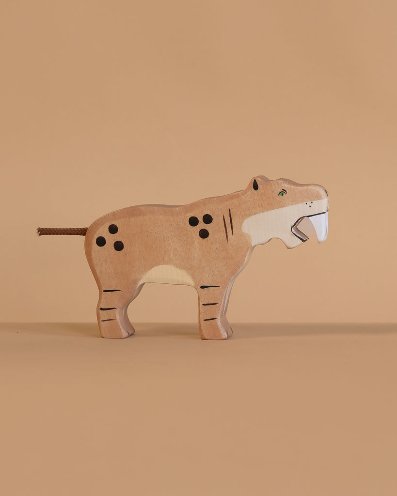 The Holztiger Saber-Toothed Tiger is a handcrafted wooden toy featuring painted spots, stripes, and white fangs. Made in Europe with great attention to detail, it stands out against a plain beige background.
