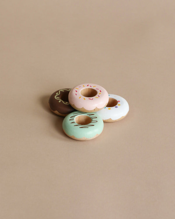 Wooden Donuts: Four pastel-iced wooden donuts in brown, pink, blue, and white with sprinkles and patterns on a beige background—perfect for imaginative play and creative role-playing fun.