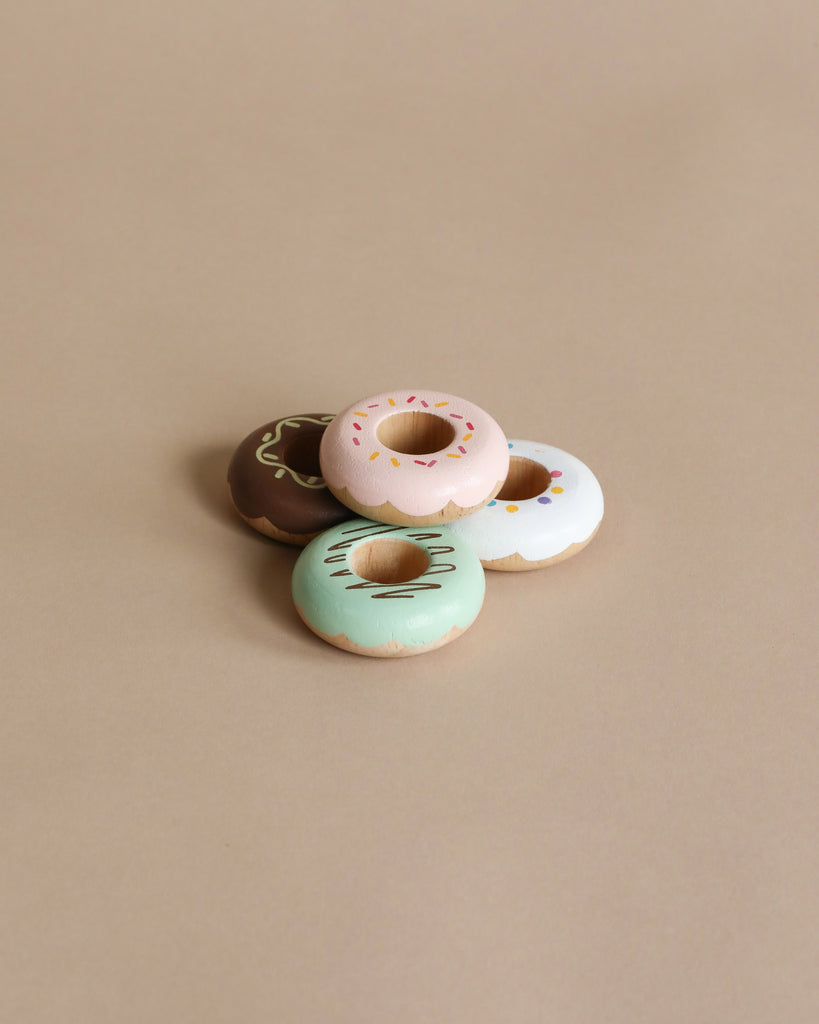 Wooden Donuts: Four pastel-iced wooden donuts in brown, pink, blue, and white with sprinkles and patterns on a beige background—perfect for imaginative play and creative role-playing fun.