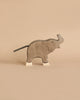 A wooden toy elephant handcrafted out of maple and beech wood stands against a beige background. The Holztiger Small Elephant, Trunk Raised, resembling HOLZTIGER figures, has a simple design with white accents on its feet and a short, black tail. Its minimalist style gives it a charming and rustic look.