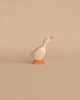 A minimalistic wooden duck figurine stands on a light beige surface against a matching beige background. This Holztiger Goose, Small is painted white with an orange beak and orange feet. Its simple design features a few subtle blue lines on its wings, embodying the charm of handcrafted wood, Made in Europe.
