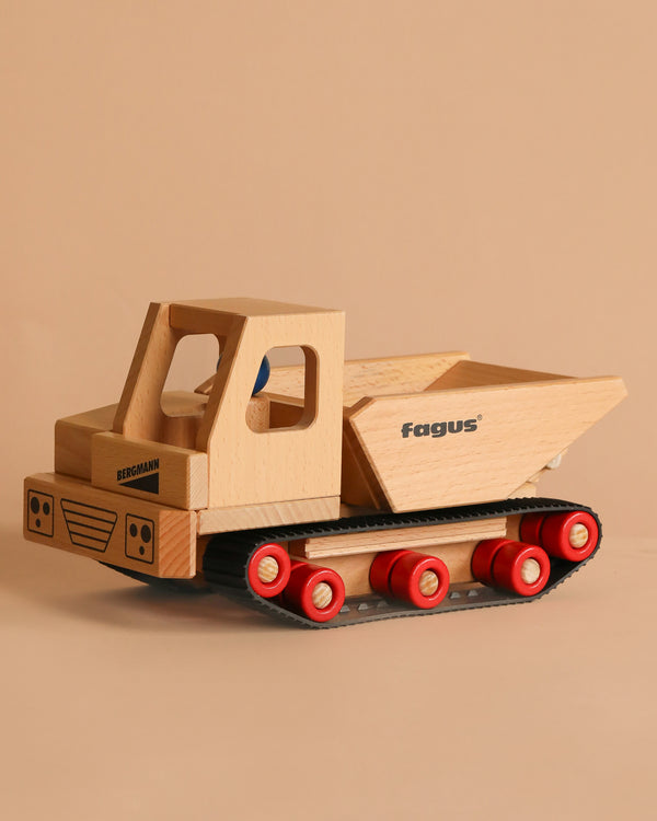 The Fagus Wooden Caterpillar Dumper, made of beech wood with red wheels, black tracks, and "Bergmann" and "fagus" printed on it, is shown against a plain beige background.