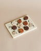 A variety of Wooden Tray Puzzles - Count to 10 Ladybugs with different designs and topping styles are neatly arranged on a rectangular ceramic plate against a beige background.