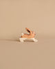 A handcrafted wooden toy rabbit painted in natural brown and white colors is shown against a beige background. The rabbit is depicted in a running pose with its ears upright and a small tail. Crafted from maple and beech wood, the delicate details of this Holztiger Rabbit, Running figure create a charming and whimsical appearance.