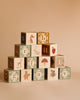 The Newborn Gift Set includes a pyramid of wooden alphabet blocks featuring letters and nature-themed illustrations—fox, rabbit, deer, bear, mushroom, flower, and strawberry—on a plain beige background.