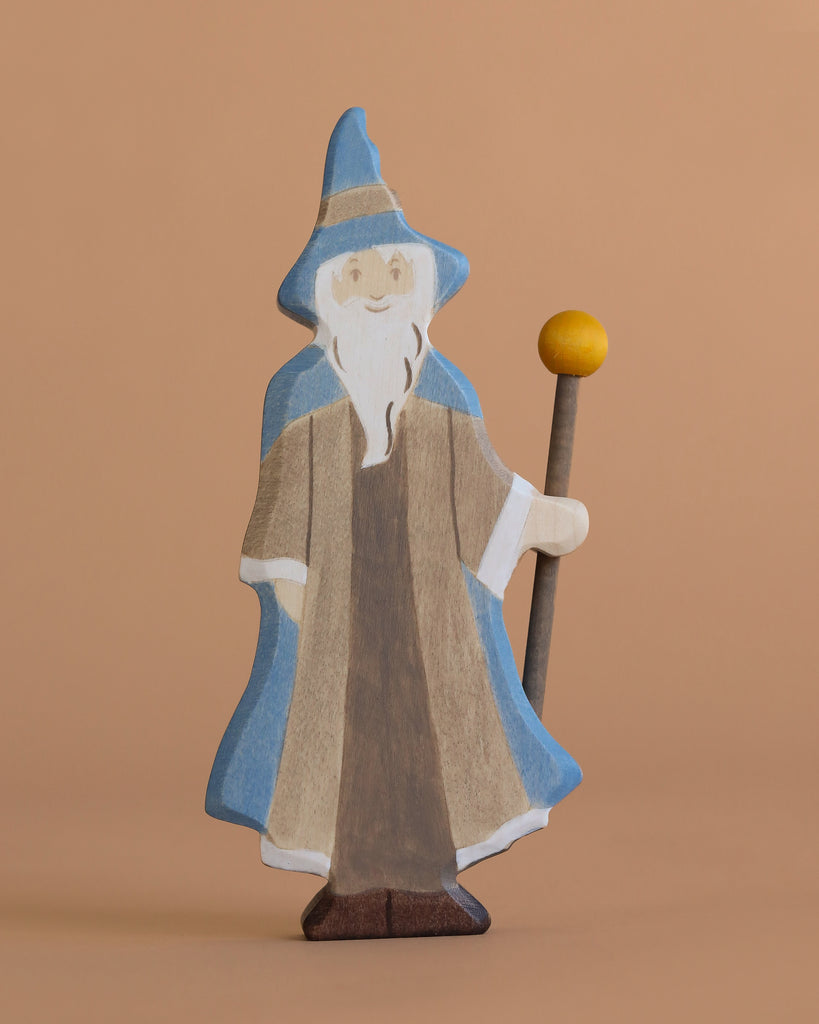 The Holztiger Magician is a handcrafted wooden figure featuring a long white beard, blue hat and cloak, brown robe, and a staff with a yellow sphere—perfect for imaginative play on any plain beige background.