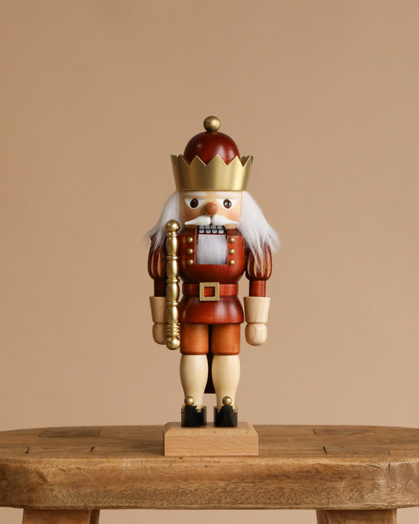 The Christian Ulbricht Collectible Wooden Nutcracker - King (Natural and Gold) stands on a rustic wooden table against a plain beige background, featuring a golden crown, gold staff, white hair, and natural finish.