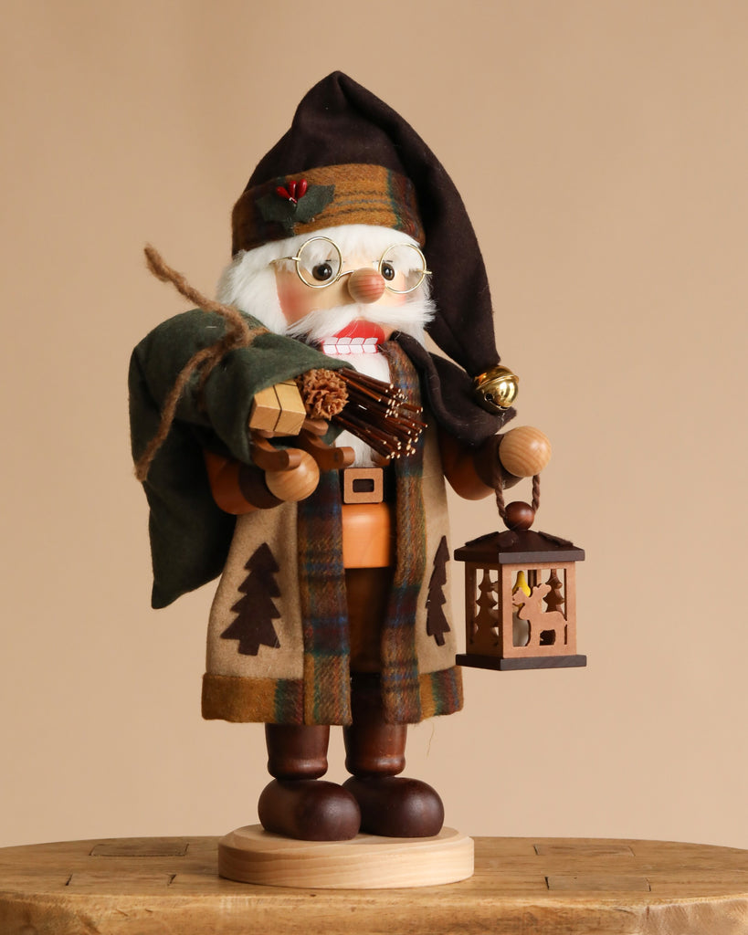 The Christian Ulbricht Collectible Wooden Nutcracker - Natural Woodsy Santa With Lantern stands on a round wooden base, wearing plaid clothes and boots, holding a green sack, firewood, and lantern. Made in Germany.