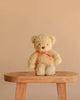 Snuggle Bunnies - Arthur the Bear, featuring a red stripe bow, sits on a wooden stool against a beige background—an ideal nursery companion or thoughtful children’s gift.