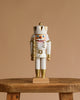 The Christian Ulbricht Collectible Wooden Nutcracker - King (White and Gold) stands upright on a rustic wooden stool, crowned and mustached, against a plain beige background.