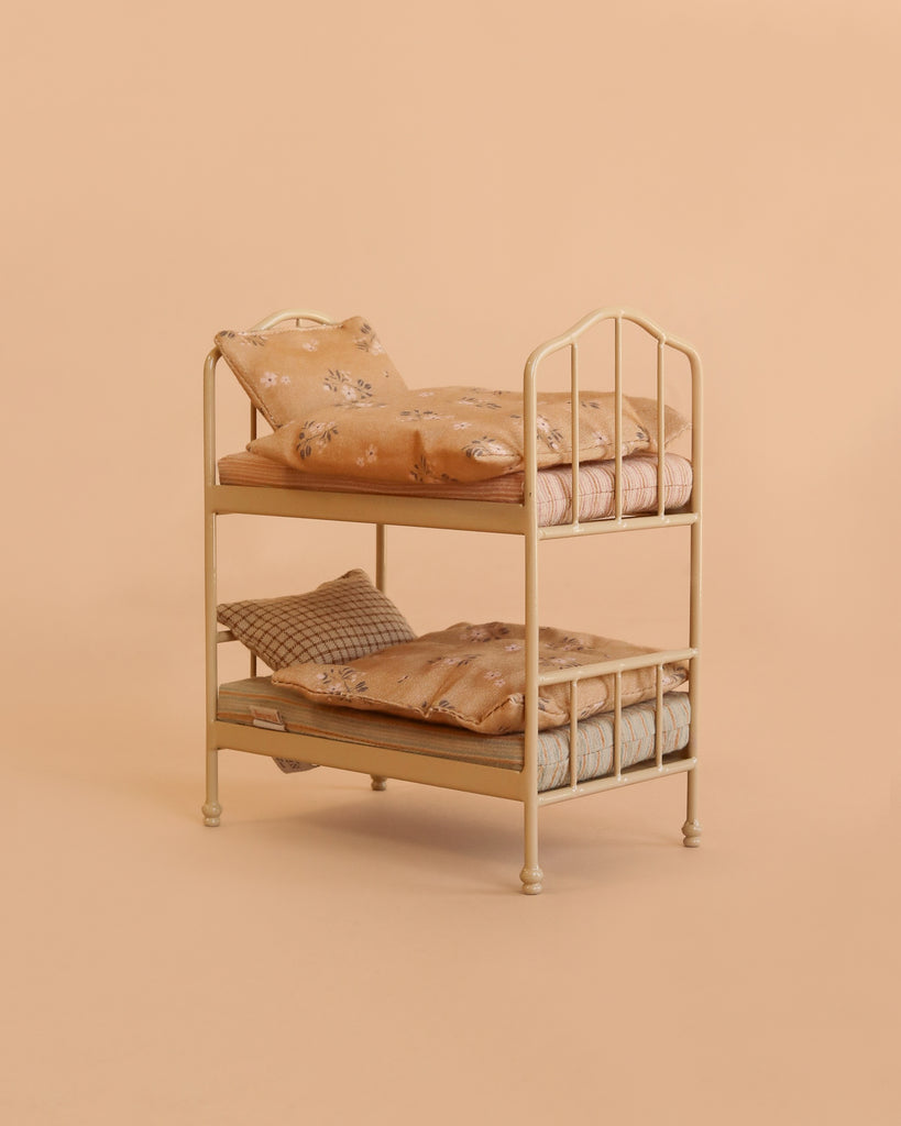 The Maileg Bunk Bed Bedroom Set with Little Brother & Sister features a small cream-colored bunk bed adorned with floral-patterned bedding and pillows, set against a plain beige background—perfect for welcoming tiny Maileg mice to a cozy night’s sleep.