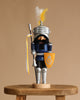The Christian Ulbricht Collectible Wooden Nutcracker - Knight Lancelot Glazed stands on a stool in blue armor, helmet with yellow and white feather plume, and holds a yellow shield and lance—an eye-catching collectible.