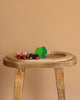 The BRIO Little Forest Train Set features a wooden toy train with red wheels on a wooden track, passing two green trees on a wooden table, all set against a plain beige background.