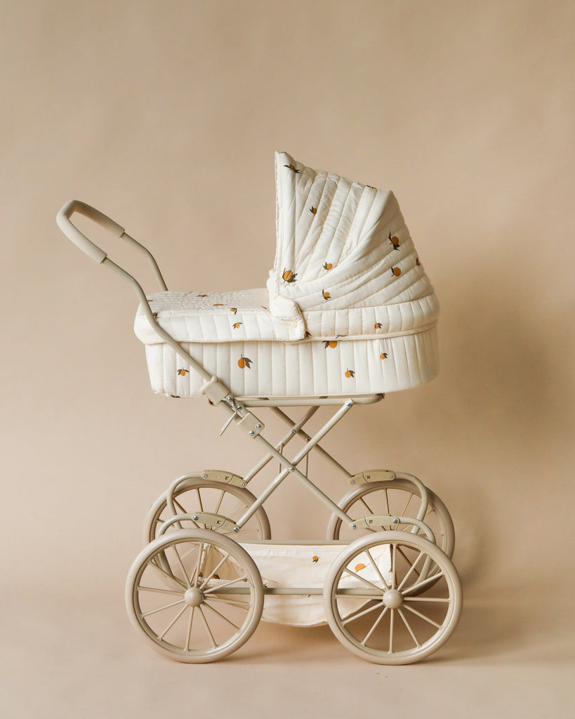 The Konges Sloejd Doll Pram - Lemon features large wheels, a curved handle, quilted fabric with small floral prints, and a hood. It includes an organic cotton mattress for comfort and comes in a neutral beige color.