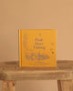 The yellow hardcover "Winnie-the-Pooh: Pooh Goes Visiting" stands upright on a rustic wooden stool against a beige background, featuring blue illustrations of Winnie-the-Pooh and friends on the cover.