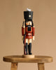 The Christian Ulbricht Collectible Wooden Nutcracker - Soldier, in a red uniform and black hat, stands on a wooden stool against a beige background.