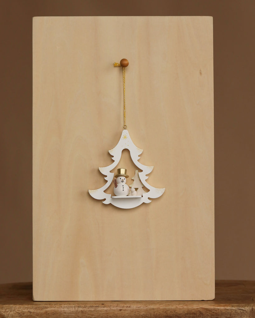 The Christian Ulbricht Ornament - White Tree with Snowman is a 3.5-inch wooden Christmas tree ornament featuring a small snowman and two trees, hanging by a gold string against a plain light wood background.