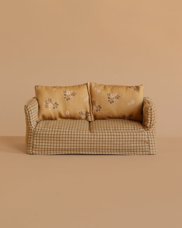 A small beige checkered Maileg Couch, Mouse - Mable, with two floral-patterned cushions, set against a plain beige background.