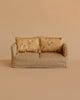 A small beige checkered Maileg Couch, Mouse - Mable, with two floral-patterned cushions, set against a plain beige background.