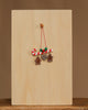 The Christian Ulbricht Ornament - Candy Cane Ornament, featuring red-and-white stripes with holly, hangs from a wooden peg beside a collectible plaque with two gingerbread people and a heart-shaped cookie on a plain wooden background.