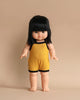 A Minikane Clothed Standing Doll (14.5") - Jade-Lou, with straight black hair and bangs, dressed in a yellow sleeveless romper with black trim, stands upright against a beige background. This anatomically correct doll has a neutral facial expression, is barefoot, and carries a gentle vanilla scent.