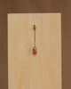 The Christian Ulbricht Ornament - Angel (Natural) is a small wooden doll charm with a painted face, hanging by a string against a light wooden panel. Made in Germany, it contains small parts and may pose a choking hazard to young children.