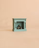 A miniature teal fireplace with a stack of logs from the Maileg Grandma’s Living Room Set, perfectly sized for a Maileg dollhouse.