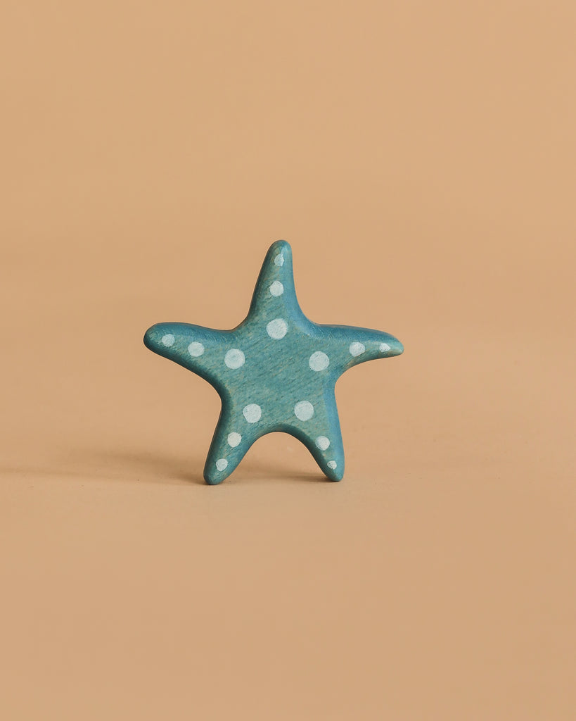 A small, blue star-shaped piece with white polka dots stands upright on a plain, light peach background—a charming figure from the Handmade Holzwald Coral Reef Set.