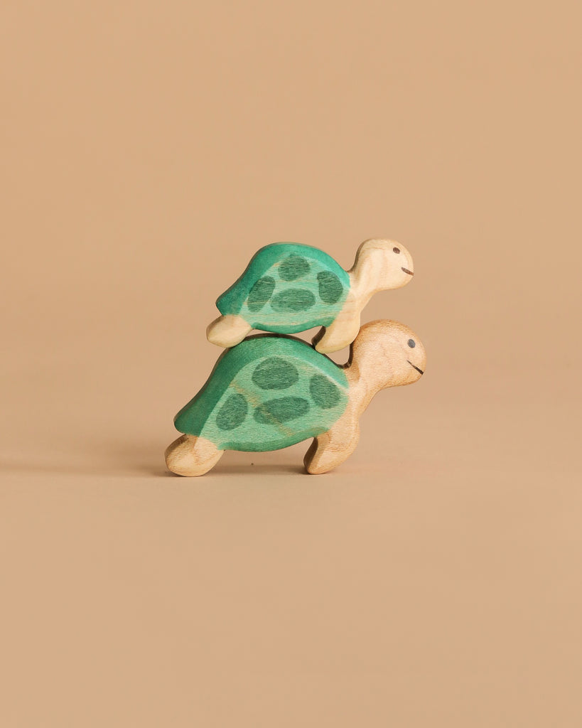 Two toys from the Handmade Holzwald Underwater World Set—wooden turtles with green shells—are stacked on each other against a beige background, showcasing the charm of handmade wooden sea creatures.