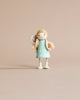 Mrs. Goodwood and her Baby, a small solid wood doll in a teal dress with polka dots and a beige scarf, holding a tiny white bear, stands against a plain light beige background.