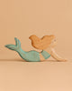 The Handmade Holzwald Mermaid features light brown hair and a greenish-blue tail, posed as if swimming against a plain beige background—perfect for inspiring open-ended play.