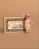 A small Maileg mouse from the Maileg Bunk Bed Bedroom Set with Little Brother & Sister, dressed in a pink outfit, stands next to a vintage-style Maileg matchbox labeled “Mouse Race” with an old-fashioned race car illustration on a tan background.