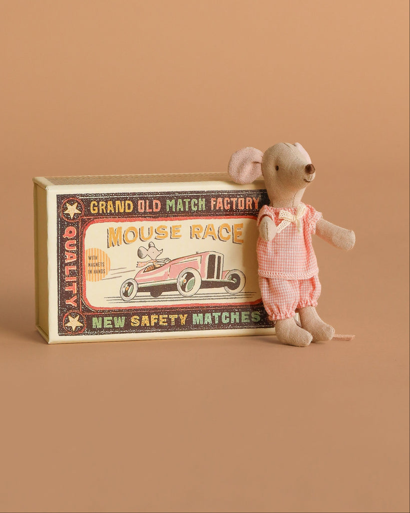 A Maileg Grandparents & Me Set is displayed beside a vintage-style matchbox labeled “Mouse Race,” featuring an illustration of a race car. The warm beige background and surface highlight the set’s charming, nostalgic appeal, reminiscent of classic Cigar Box toys.
