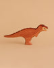 The Handmade Holzwald T-Rex Maroon, a sustainable wooden dinosaur figurine, stands upright on a light beige background. Painted in maroon and brown with green eyes and white teeth, it features a slightly open mouth.