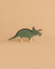 A Handmade Holzwald Triceratops, painted green and beige, stands on a plain peach background—ideal for anyone looking for sustainable wooden toys.