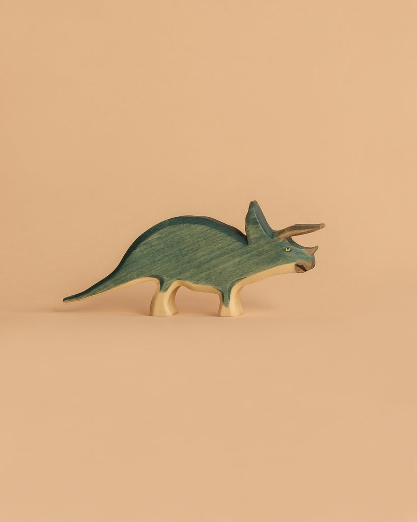 A Handmade Holzwald Triceratops, painted green and beige, stands on a plain peach background—ideal for anyone looking for sustainable wooden toys.