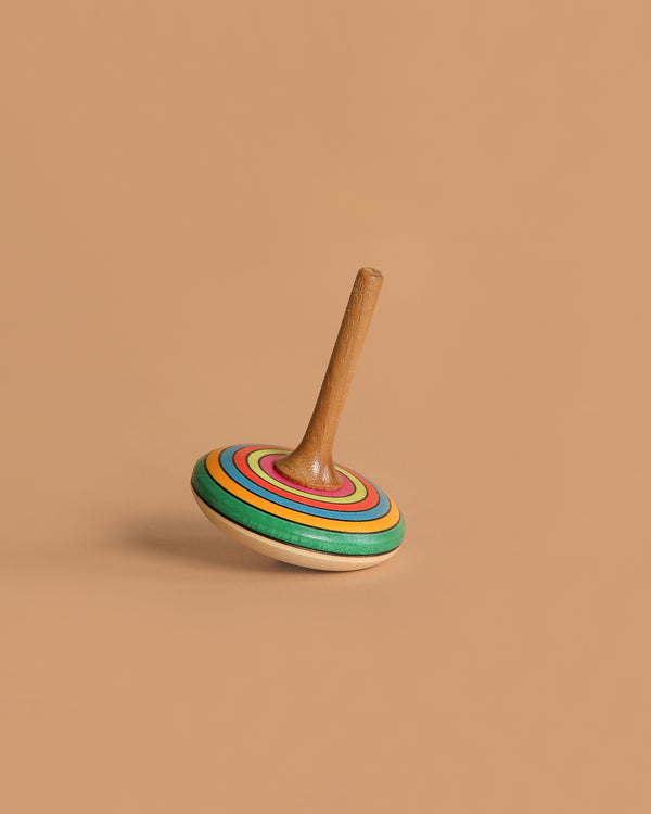 The Mader Small Spinning Top - Striped features vibrant green, blue, orange, and red rings on wood. Resting upright on a light brown background, it's a charming handmade toy perfect for Montessori-inspired playful learning.