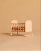 The Maileg Cradle, My - Light Rose, featuring floral bedding, sits atop a beige surface with a matching beige background.