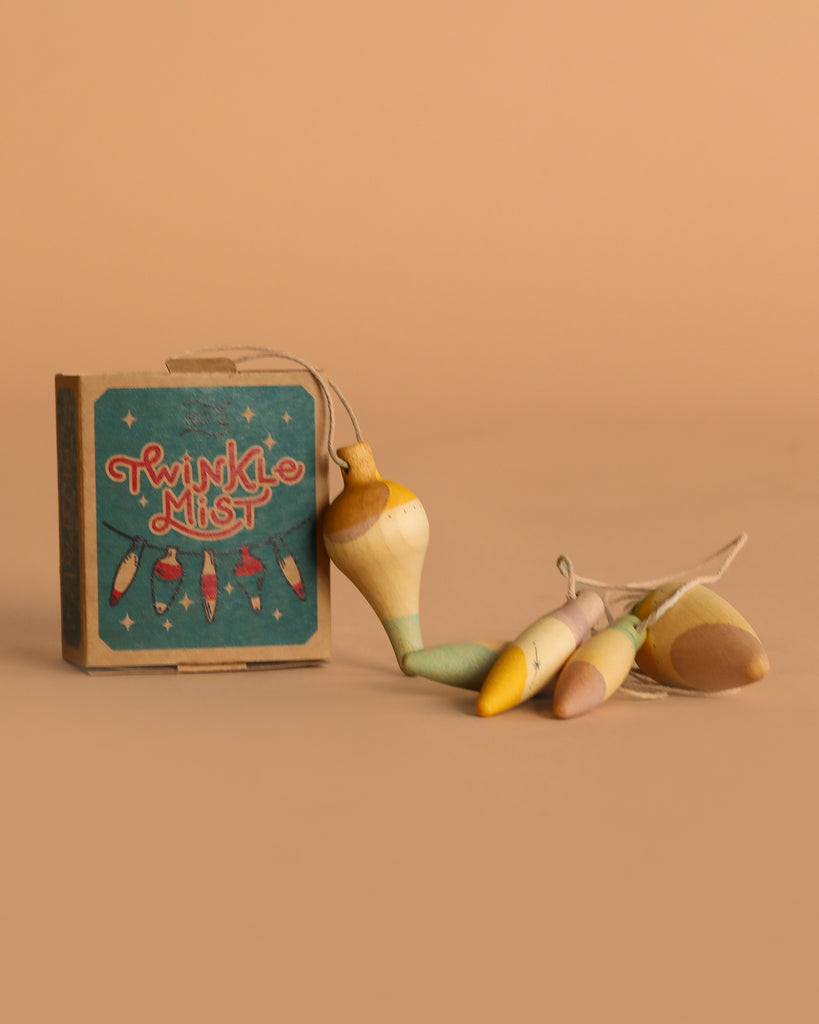 A small Grapat Ornament Set - Twinkle Mist sits by four pastel wooden fishing bobbers tied with string—charming handmade ornaments ideal for holiday décor—arranged on a beige background.