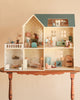 The Maileg Fully Furnished Dollhouse Set + Surprise Gift, featuring six beautifully appointed rooms with vintage-style furniture and charming animal figurines, is displayed on a wooden table against a beige background.