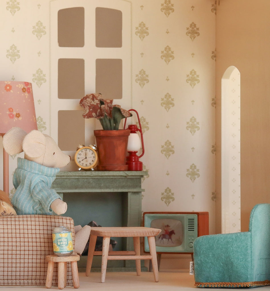 The Maileg Fully Furnished Dollhouse Set + Surprise Gift features a toy mouse in a blue sweater sitting on a sofa in a cozy, vintage-style miniature living room complete with a lamp, clock, table, plant, and TV.