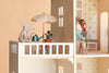 Stuffed toy mice are arranged in the Maileg Fully Furnished Dollhouse Set + Surprise Gift, with one perched on a balcony holding a watering can and tending to a potted plant under a striped umbrella, while another relaxes inside near miniature toy furniture.