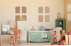 A toy mouse cooks in a miniature vintage kitchen beside a green stove, while a nearby table displays milk, a bowl, and bread. Toy food is scattered across the floor, capturing the charm of a Maileg Fully Furnished Dollhouse Set + Surprise Gift and its delightful dollhouse miniatures.