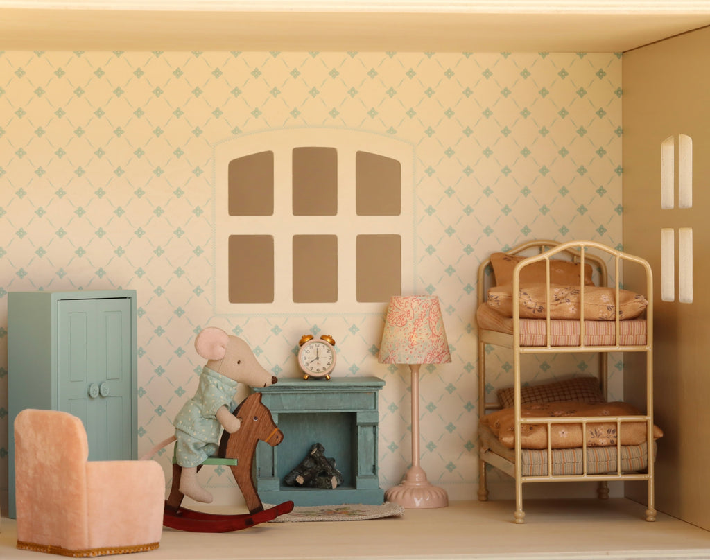 Transform your playtime with the Maileg Fully Furnished Dollhouse Set + Surprise Gift, featuring an adorable toy mouse on a rocking horse, a cozy bunk bed, a blue cabinet, a pink chair, and warm lighting from an elegant lamp. The room is perfectly detailed with a clock on the mantle and beautifully patterned wallpaper surrounding the window—ideal inspiration for miniature enthusiasts and those who love assembling dollhouse scenes.