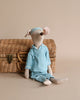 Maileg Maxi Mouse in Pyjamas, your perfect rest-time companion, is dressed in a blue striped pajama set with a matching nightcap. Seated against a wicker basket with a clasp, this charming stuffed toy stands out beautifully against the plain light beige background.