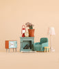 Bring a cozy touch to your miniature collection with the Maileg Family Room Set, featuring dollhouse accessories that include a teal armchair, small yellow stool, vintage TV, fireplace, rug, potted plant, clock, red lantern, and lamp. Perfect for creating charming scenes with Maileg or Maileg mouse furniture against a plain beige background.