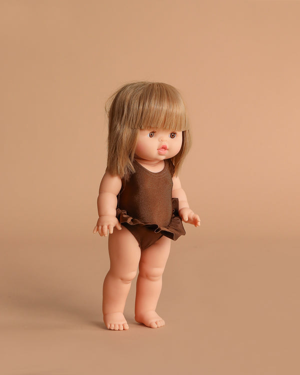 The Minikane Standing Doll (14") - Zoelie With Clothing features straight, light brown hair with bangs, a brown swimsuit, and stands barefoot against a peach background. This charming doll is made in Spain.
