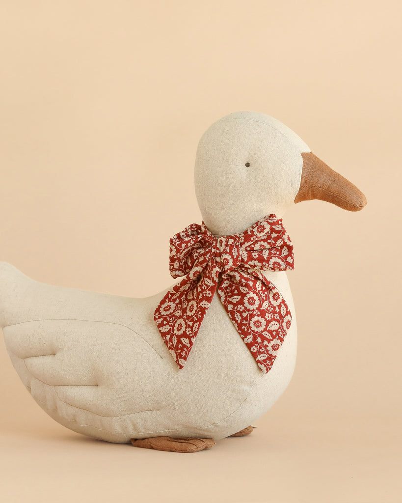 The Maileg Duck with Bow - Sand is displayed against a plain beige background, featuring soft beige fabric, a brown beak and feet, and a red patterned bow around its neck—making it a charming Christmas decoration that brings an authentic and cozy holiday atmosphere to your home.