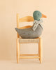 The Maileg Duck with Bow - Grey, featuring a green head, orange beak, and floral bow, is perched on a light wooden chair against a beige background—making it a charming Christmas duck decoration that brings an authentic festive atmosphere to your seasonal animal collection.