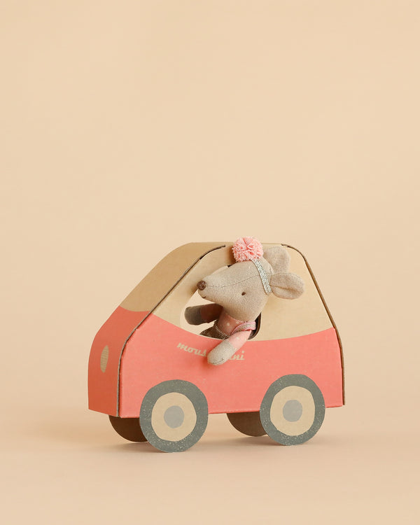 The Maileg Driver Mouse, Little Sister, wearing a headband with a pink flower, sits inside a red and beige mouse car with round gray wheels against a plain beige background.